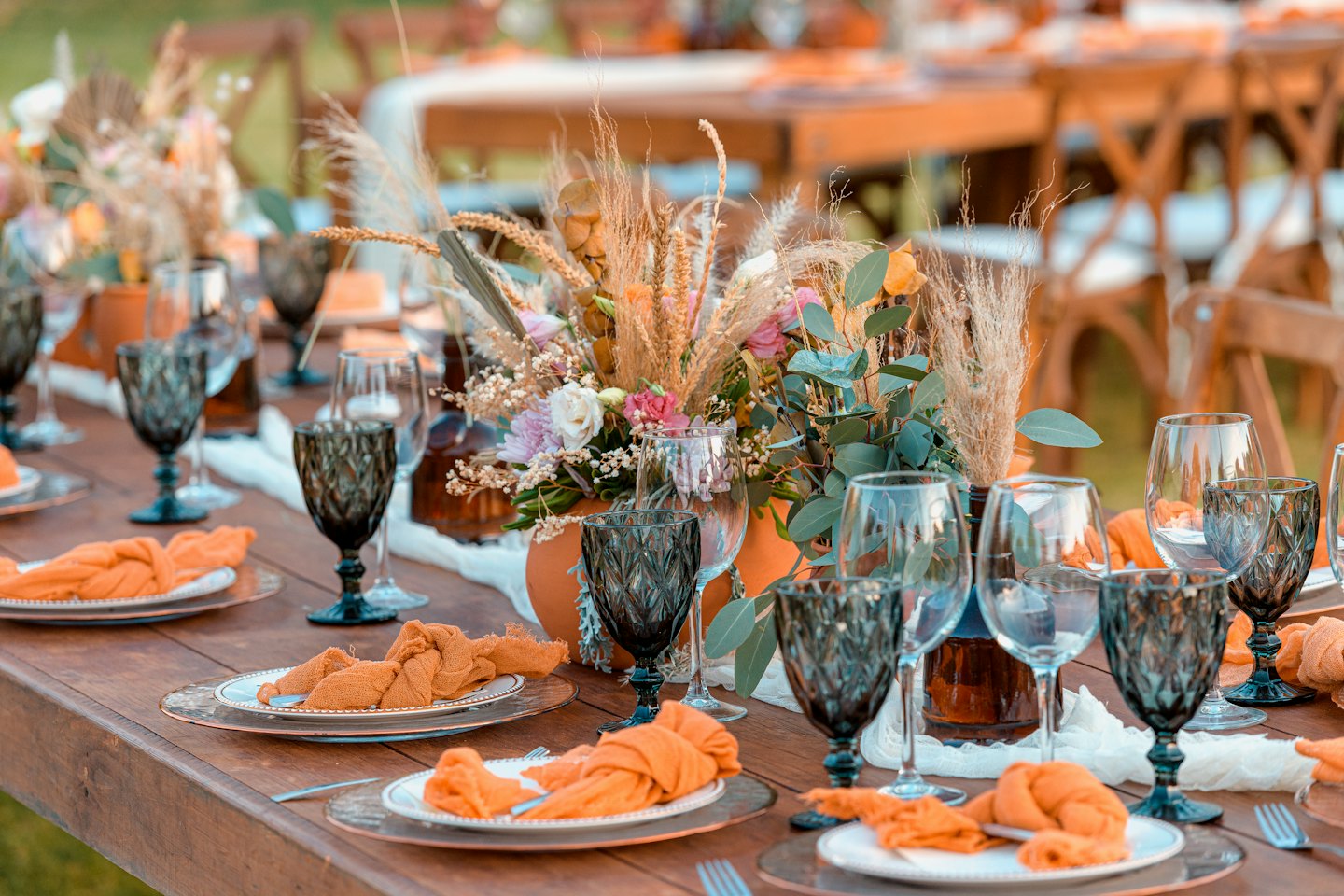 Outdoor wedding reception table set with rustic place settings and floral arrangements.