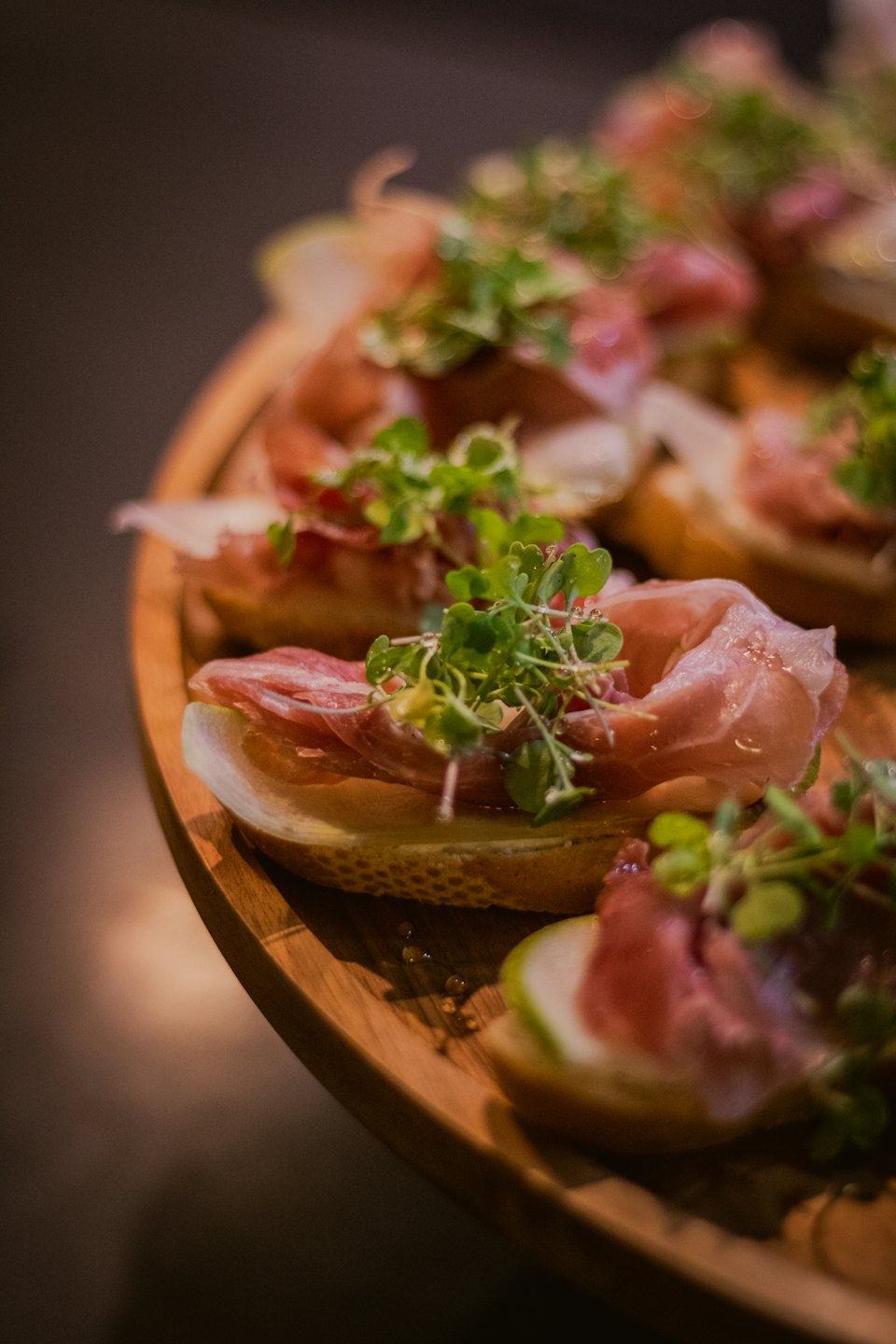 Cured meat and microgreen crostini on a wooden board.