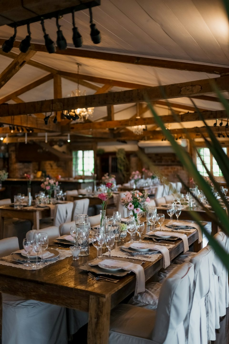 A long wooden table is set for an event with floral arrangements.