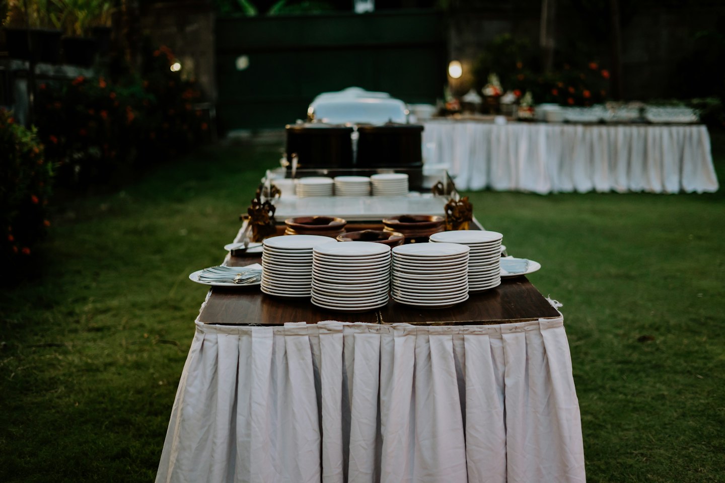 Catering buffet setup on a green lawn with white plates and serving bowls.