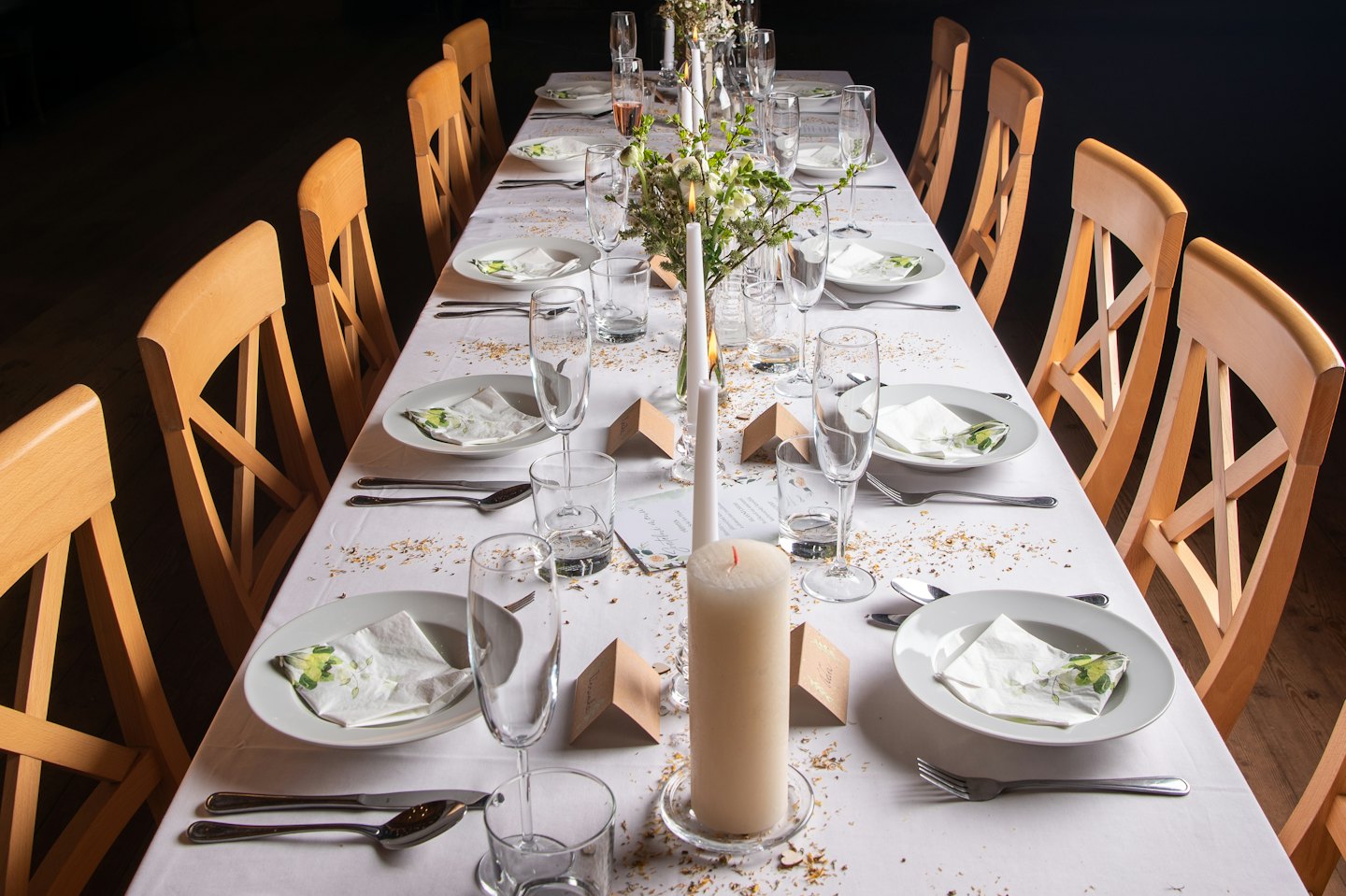 A long dining table set with white plates, glassware, and candles.