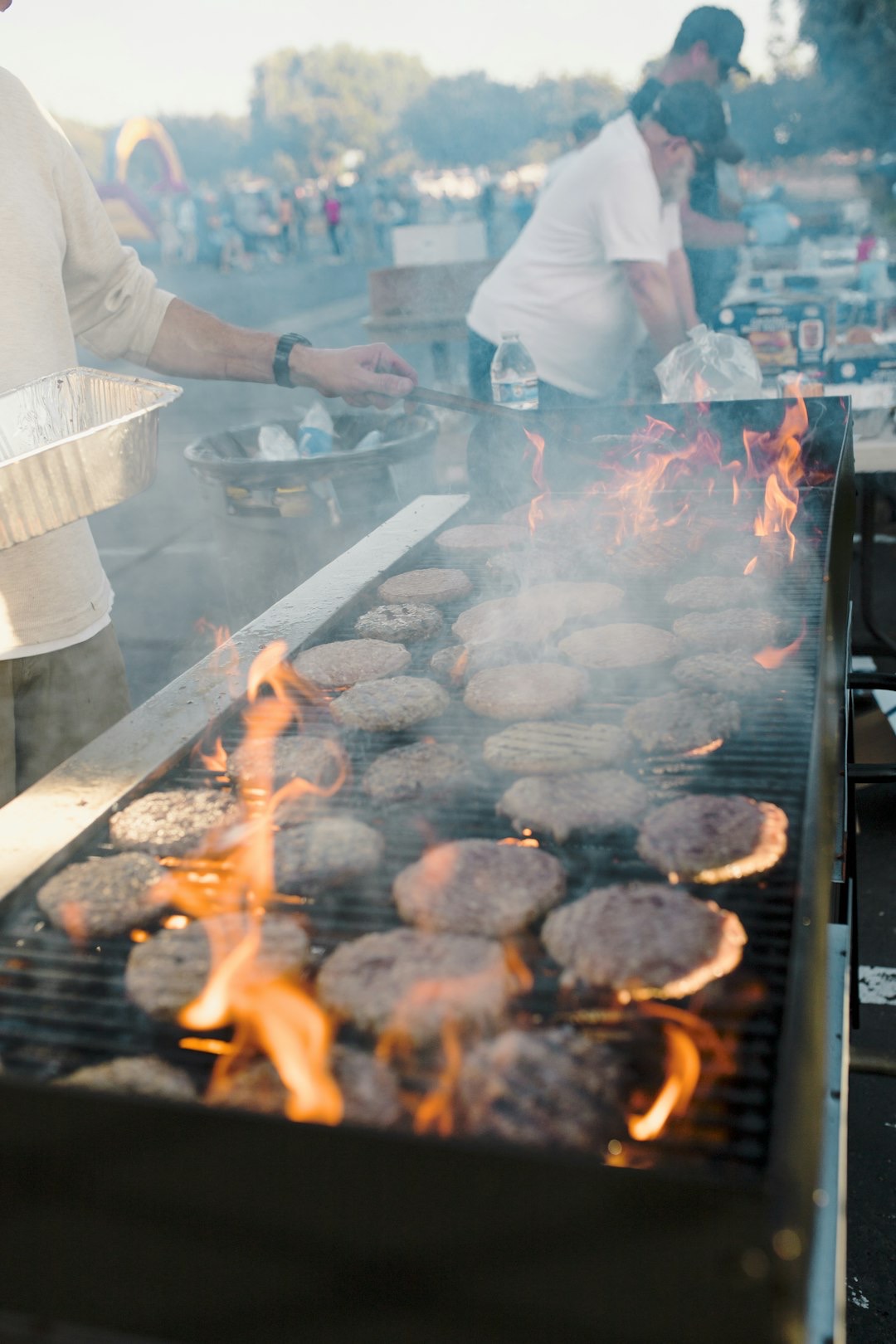 A person grills beef patties on an outdoor barbecue.